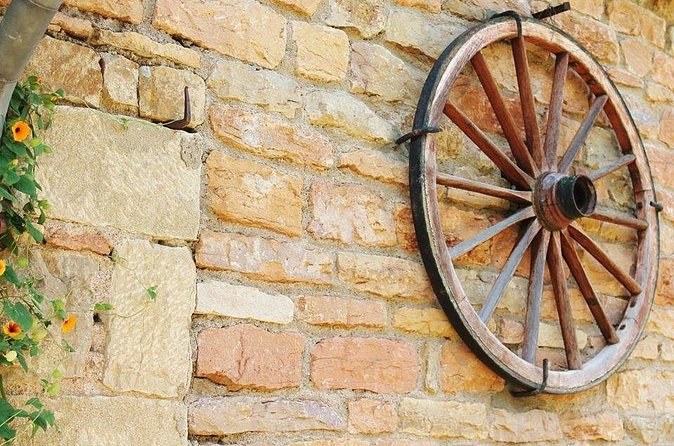 An old wooden cart wheel hung on a wall of ochre stone
