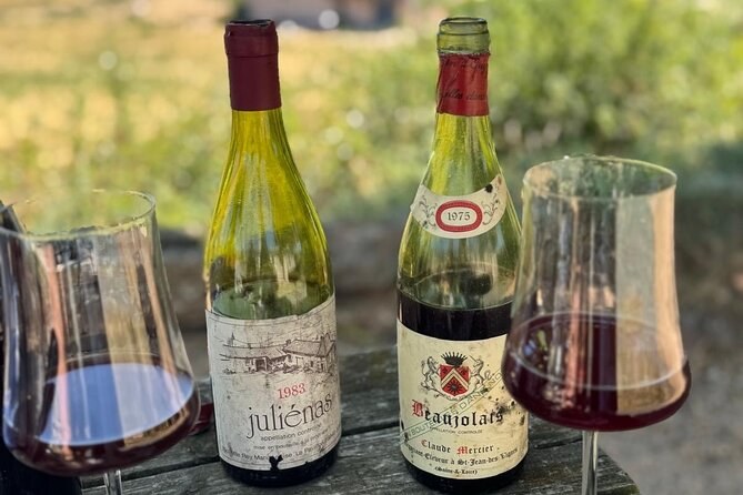 Old bottles of Juliénas and Beaujolais beside two glasses of red wine